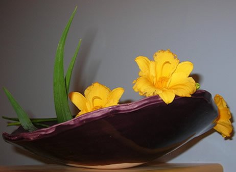 royal purple bowl with yellow daylilies against a blue wall